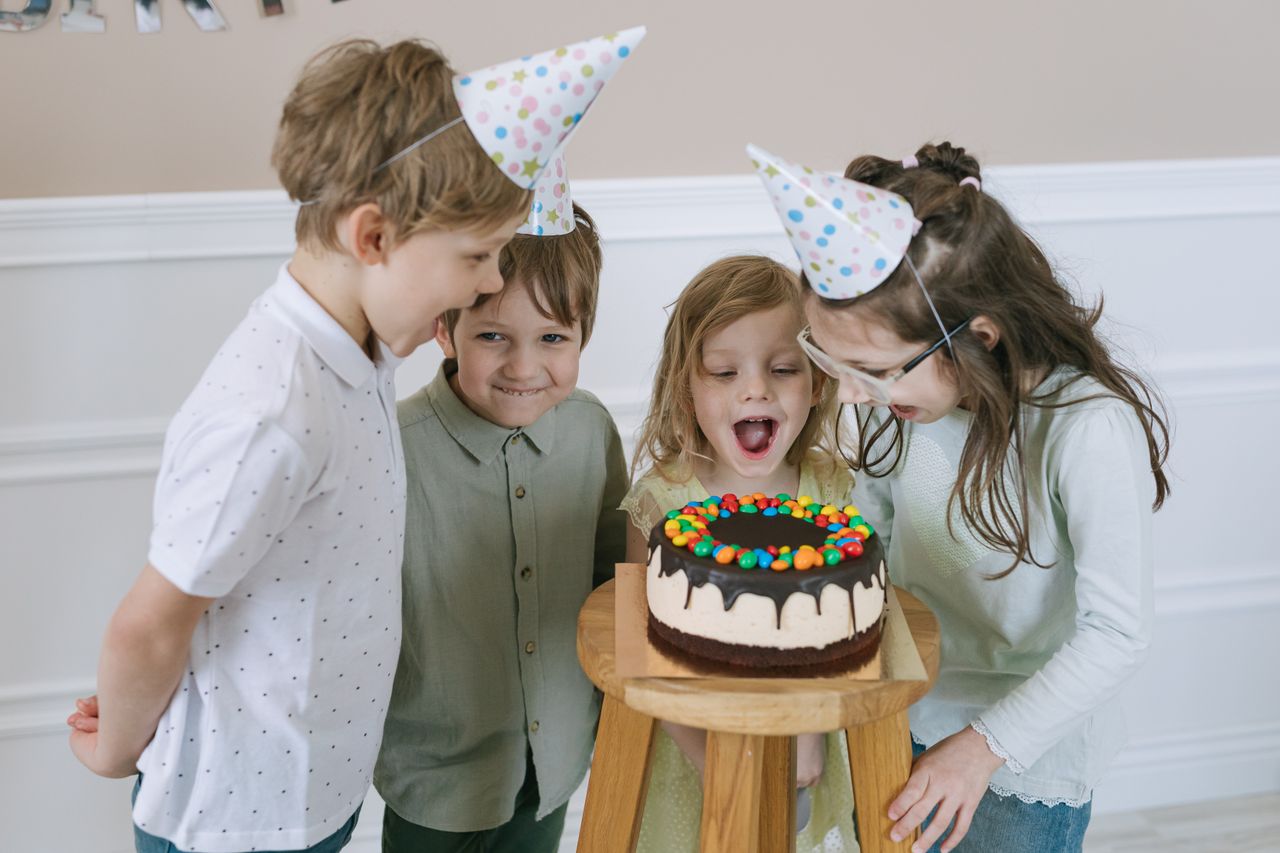 Group of children enjoying a birthday party with cake and party hats indoors.