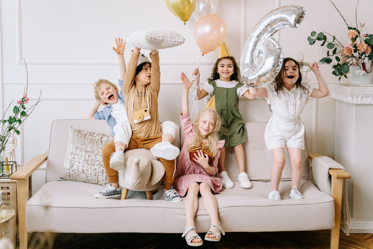 Happy kids celebrating a birthday with balloons and excitement on a living room sofa.